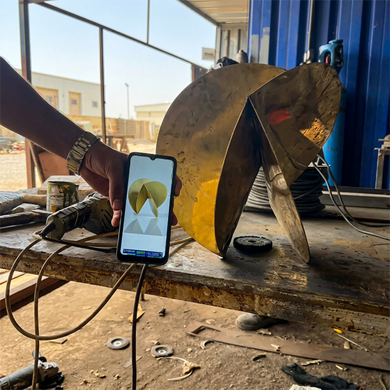 Artisan comparant une sculpture en laiton brute à son modèle 3D sur smartphone en atelier