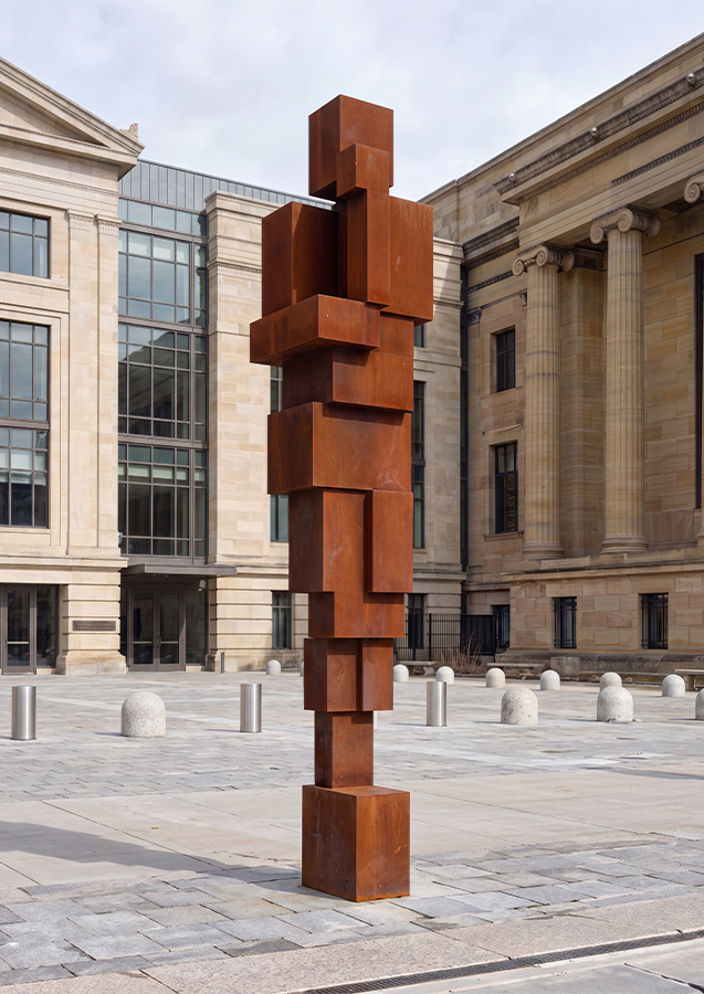 Sculpture monumentale verticale en acier Corten installée sur une place publique architecturale